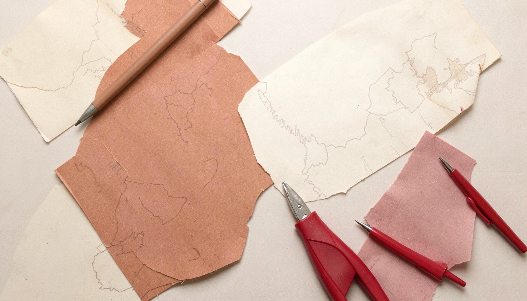 Soft overhead flat-lay photograph of warm-toned paper textures, ink pens, and faint map outlines in muted cream, terracotta, and dusty pink colors, evoking a quiet archival mood.